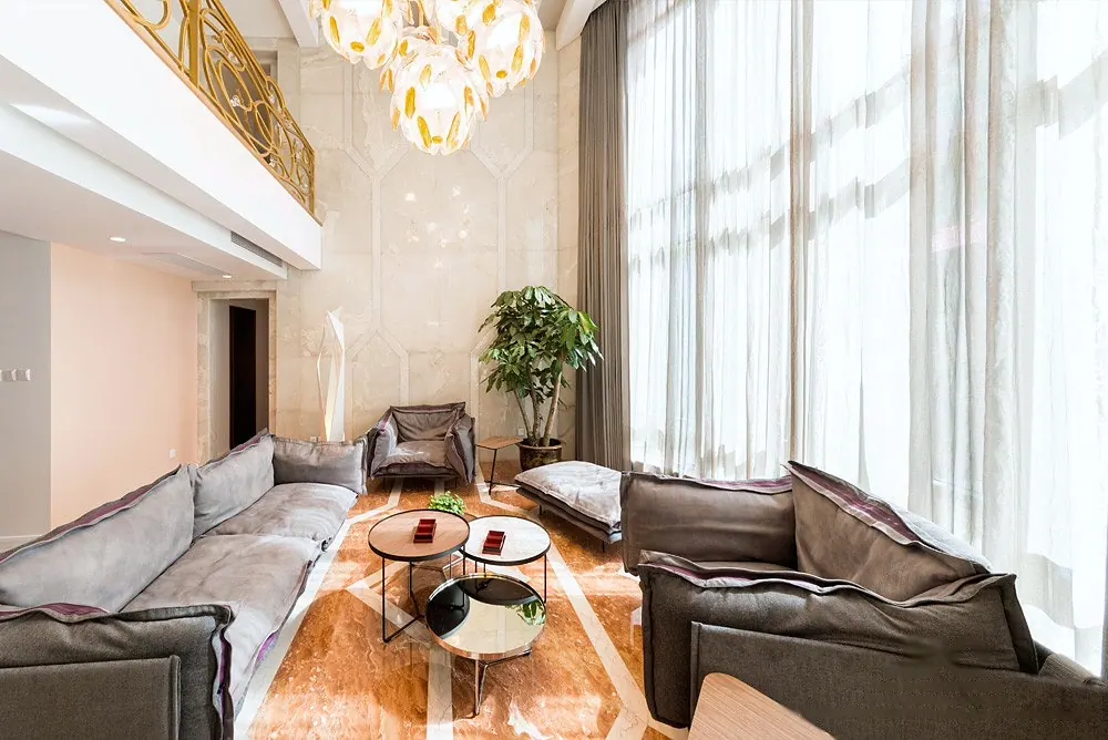 Double-height living room with grey sofas, round tables and tall curtained windows, 4 Seasons Villa
