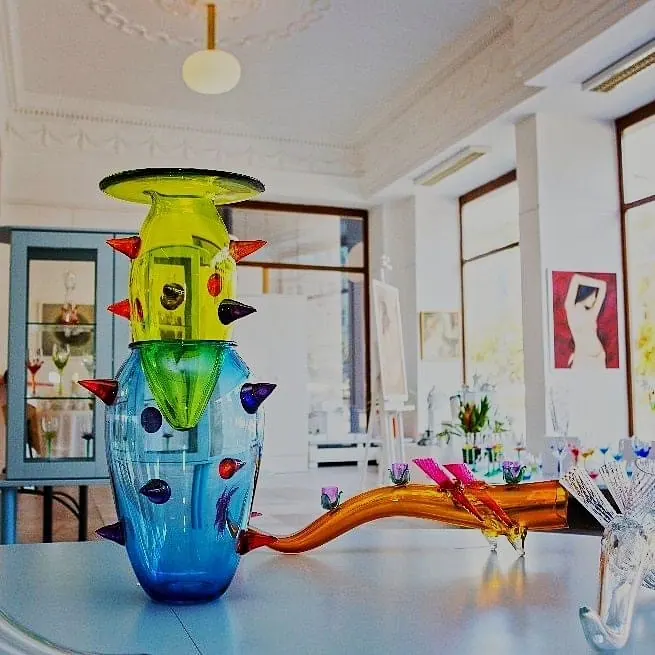 Colourful spiked glass vase and an orange glass piece on a table in a bright gallery room