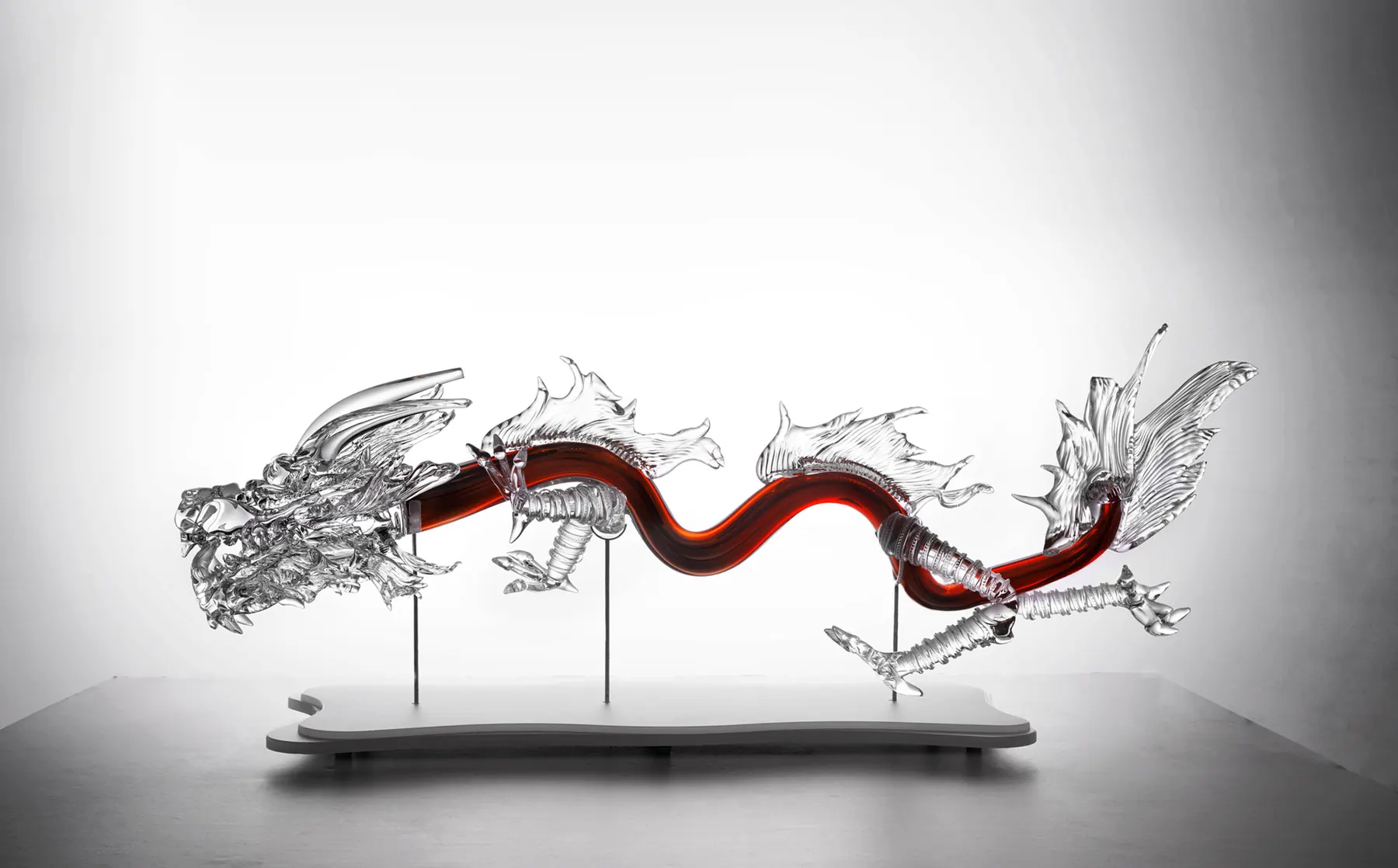 Long clear crystal dragon with a wavy red-amber body mounted on a low stand, Flying Dragon