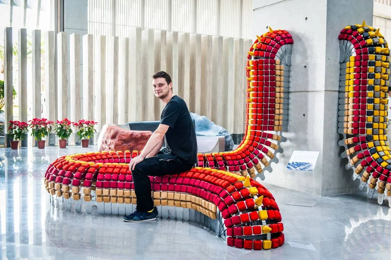 A man seated on a long curving bench of red and yellow blocks, Mangrove Tree Hotel