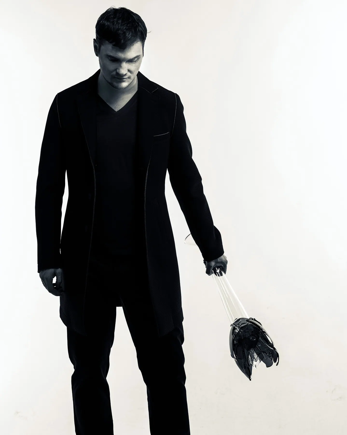 Milan Šípek dressed in black against a white backdrop, holding a dark glass object upside down