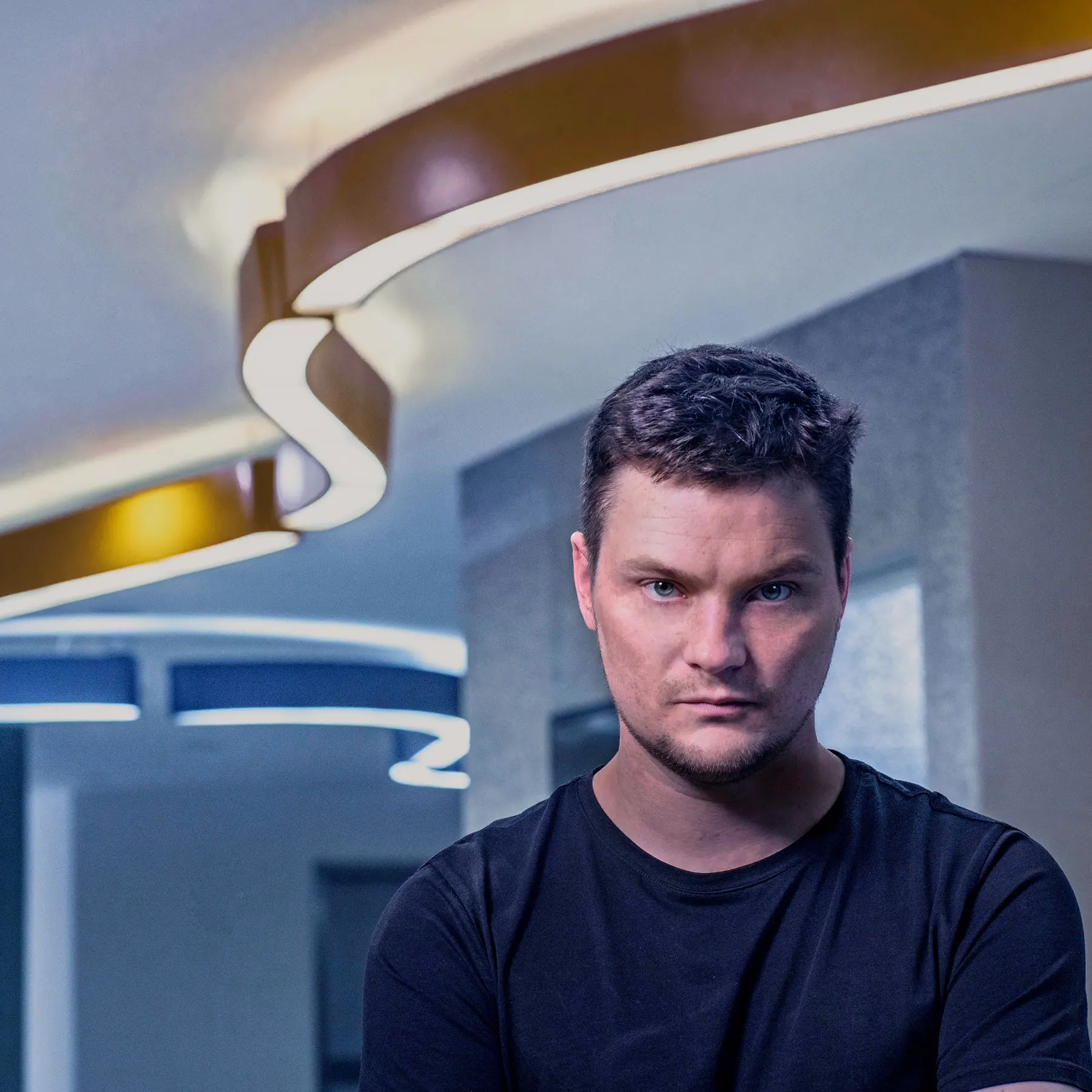 Portrait of Milan Šípek beneath a curving ribbon-shaped ceiling light