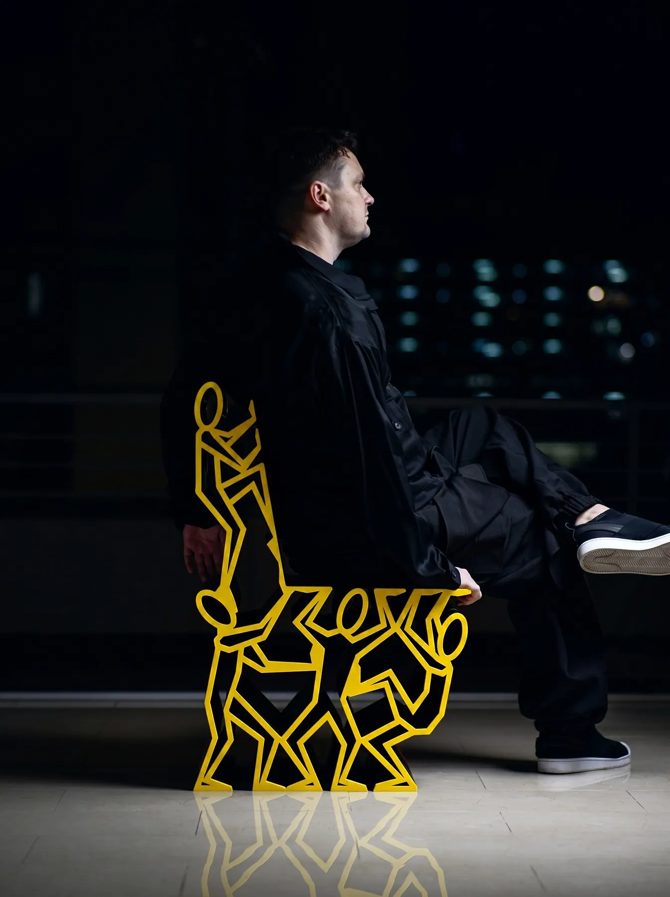 A man seated on a yellow chair formed from linked stick figures, Peeps Chair