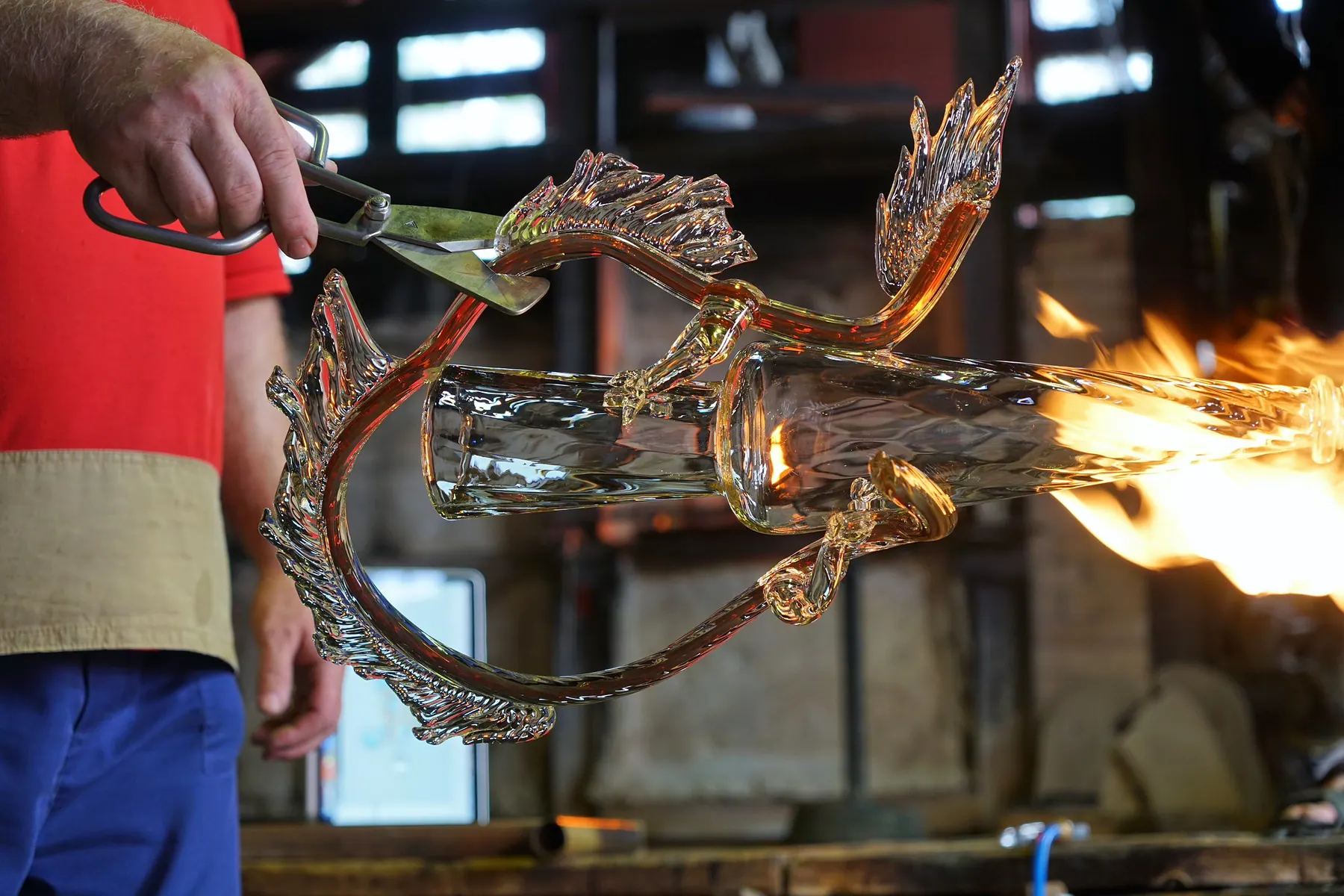 Glassmaker trimming a hot glass ornament with shears beside a torch flame, Sipek Crystal