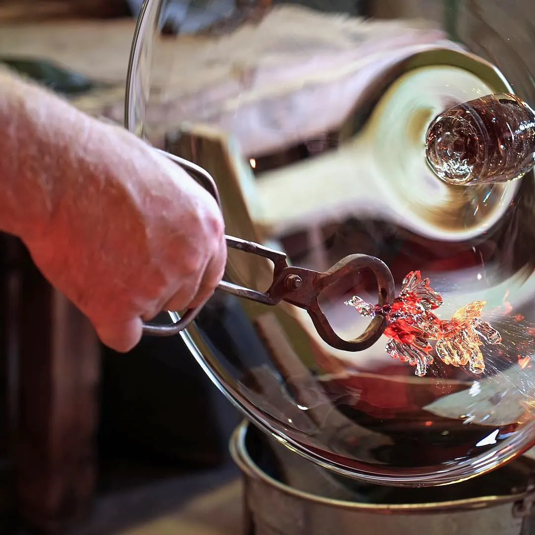 Hand with tongs shaping a red hot-glass decoration on a large clear glass piece, Sipek Crystal