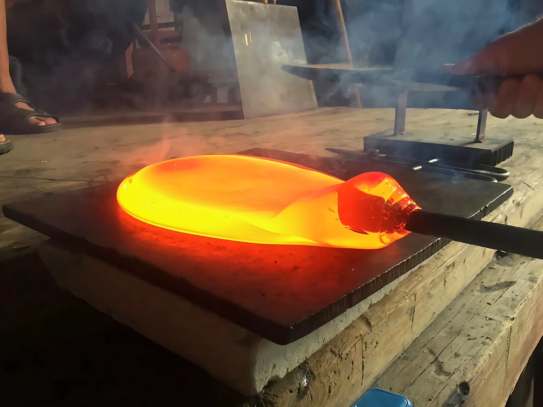 Glowing molten glass on a blowpipe resting on a metal plate in the workshop, Sipek Crystal