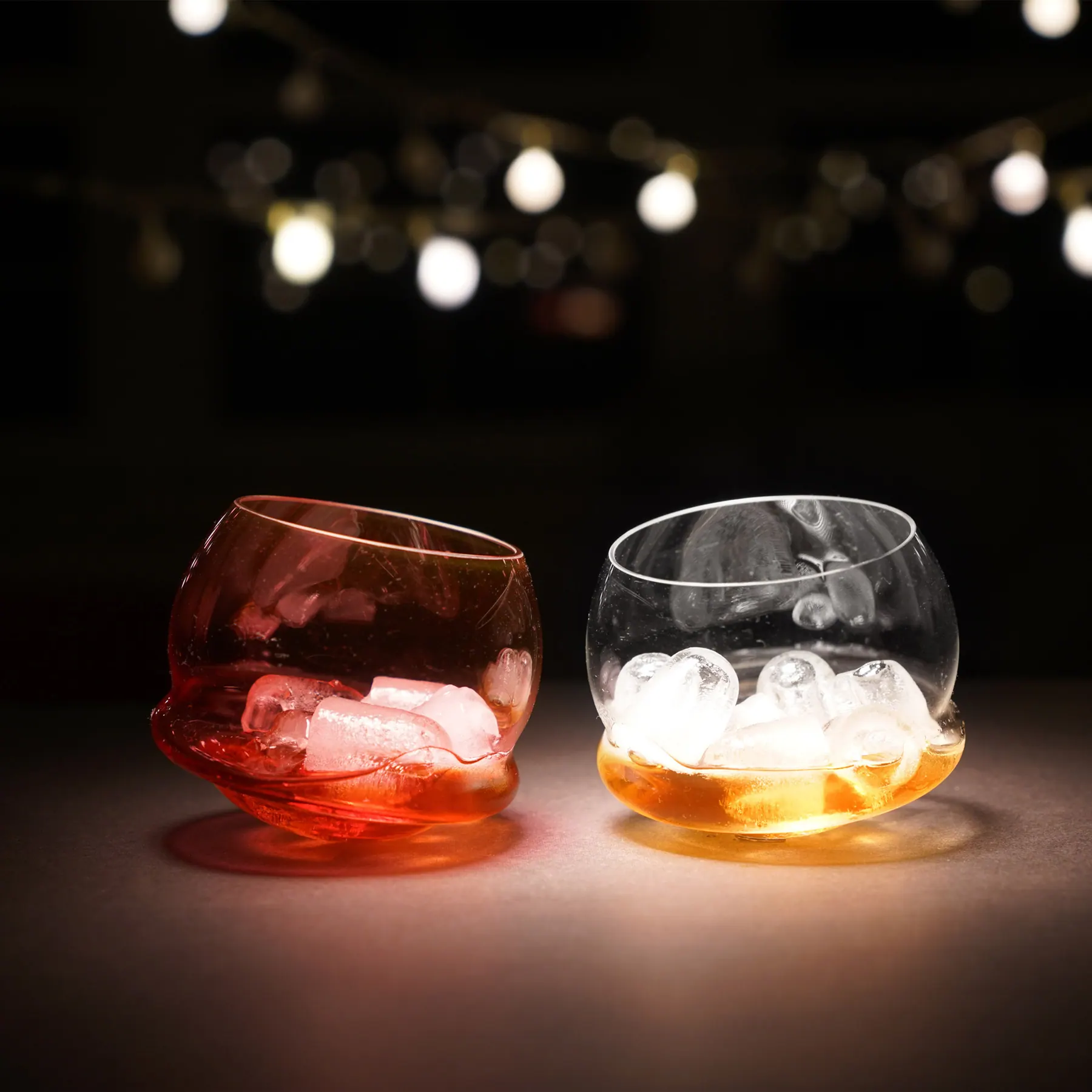 Red and clear glasses with ice and an amber drink under string lights, Tipsy glass collection