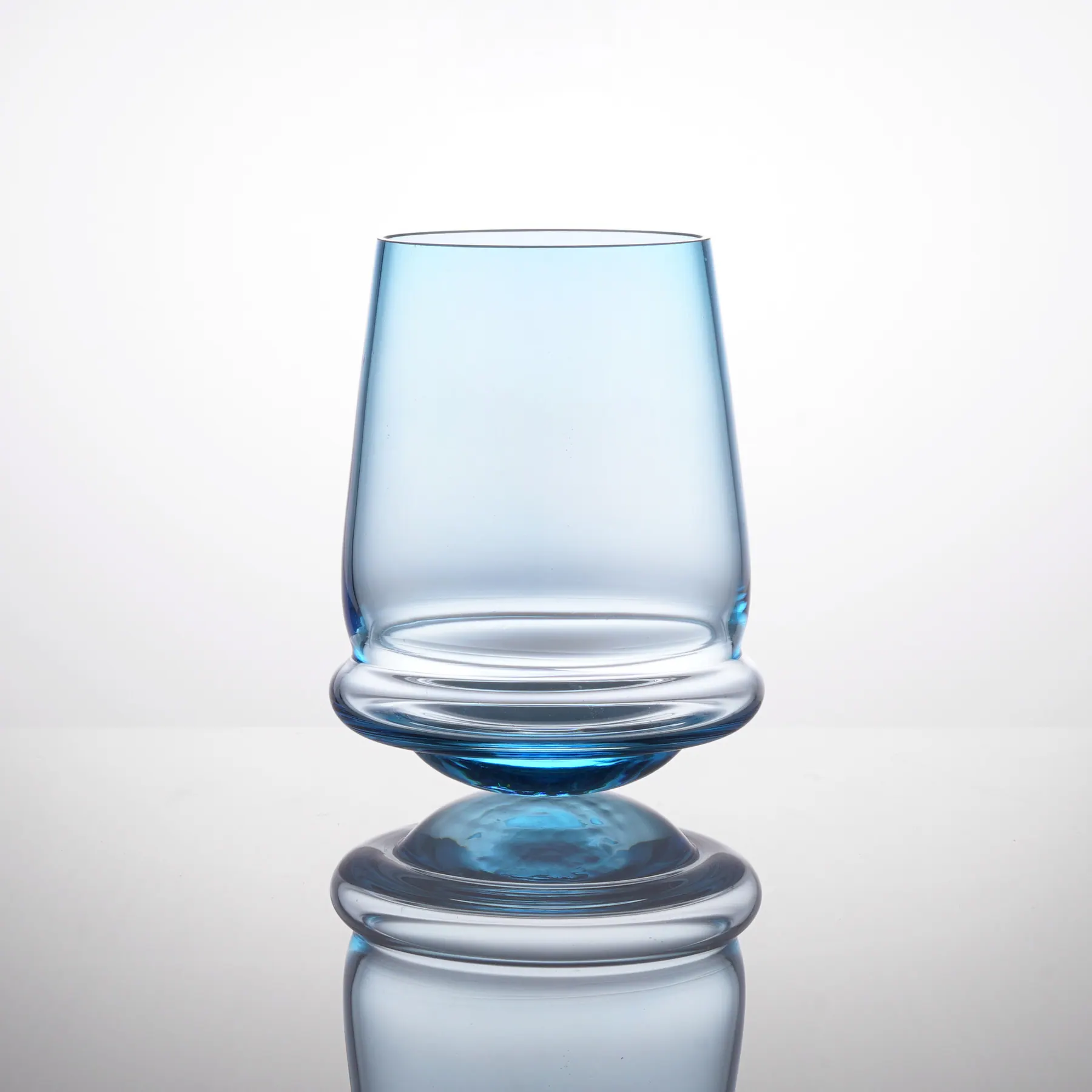 Upright light-blue glass on its rounded base, Tipsy glass collection