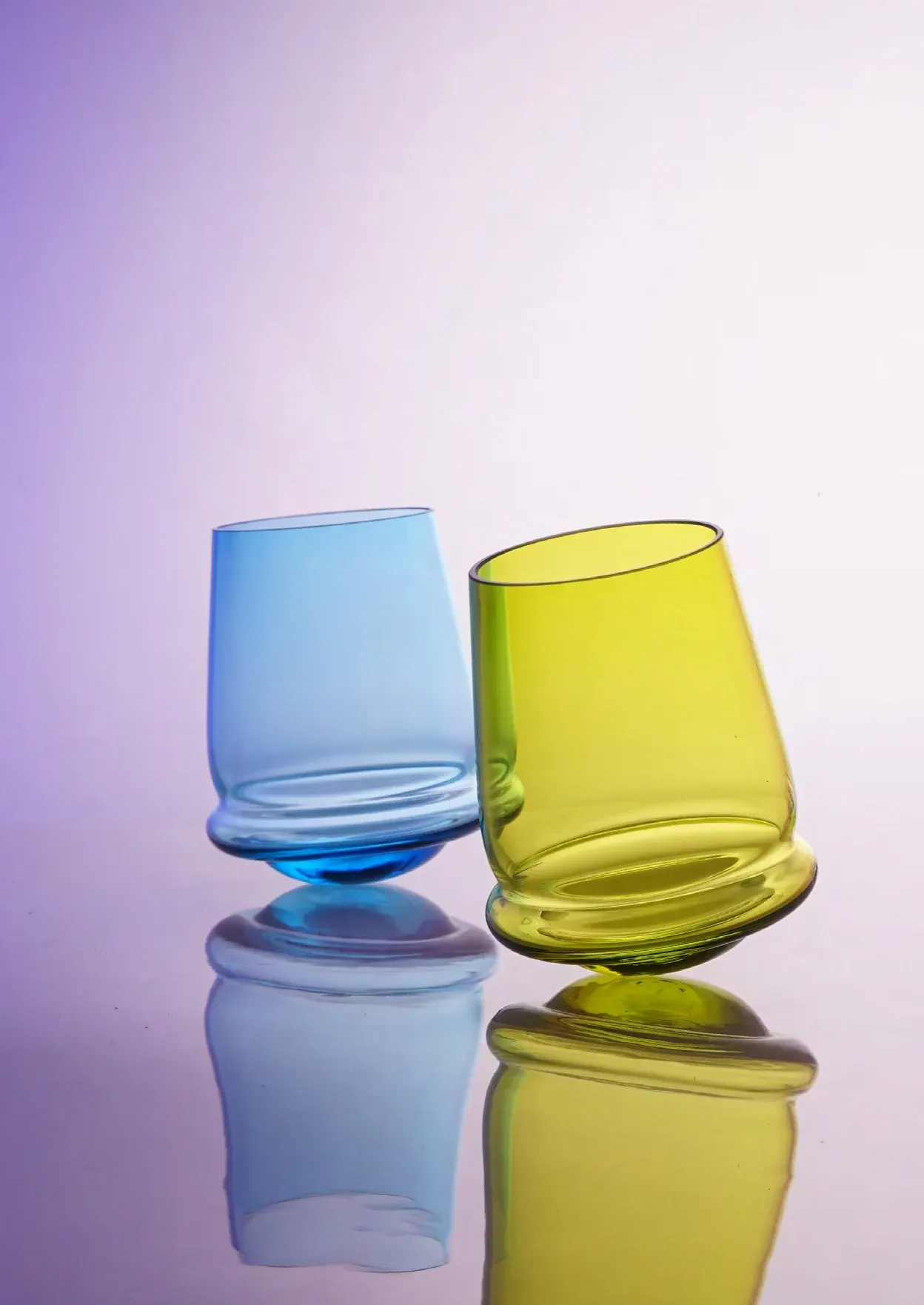 Blue and yellow-green glasses leaning together on a lilac background, Tipsy glass collection